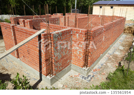Brick walls are rising at a construction site, supported by wooden forms and metal rods. Brick walls are rising at a construction site, supported by wooden forms and metal rods. 135561954