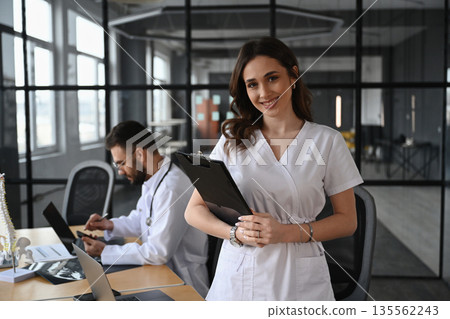 Notepad is in hands. Two doctors are in the office 135562243