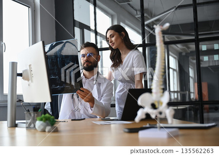 By the table with monitor, holding x-ray. Two doctors are in the office By the table with monitor, holding x-ray. Two doctors are in the office 135562263
