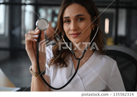 Cheerful, holding stethoscope. Woman doctor is in the office Cheerful, holding stethoscope. Woman doctor is in the office 135562314