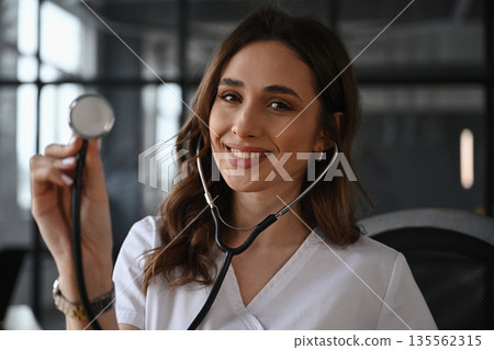 Cheerful, holding stethoscope. Woman doctor is in the office Cheerful, holding stethoscope. Woman doctor is in the office 135562315