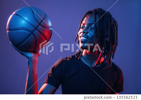 Dark room, basketball ball. African American guy is studio with neon lighting Dark room, basketball ball. African American guy is studio with neon lighting 135562515