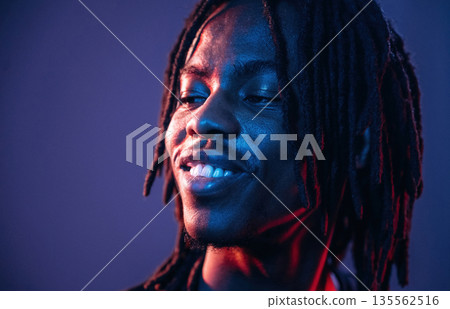Smiling, positive facial expression. African American guy is studio with neon lighting 135562516
