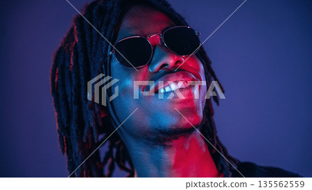 In sunglasses. African American guy is studio with neon lighting In sunglasses. African American guy is studio with neon lighting 135562559