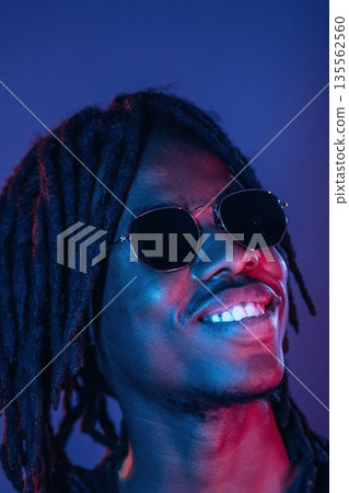 In sunglasses. African American guy is studio with neon lighting In sunglasses. African American guy is studio with neon lighting 135562560