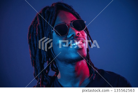 In sunglasses. African American guy is studio with neon lighting In sunglasses. African American guy is studio with neon lighting 135562563