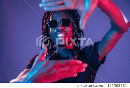 Gesture of capturing the photo. African American guy is studio with neon lighting 135562581