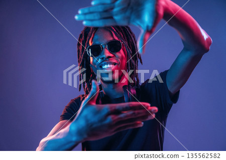 Gesture of capturing the photo. African American guy is studio with neon lighting 135562582