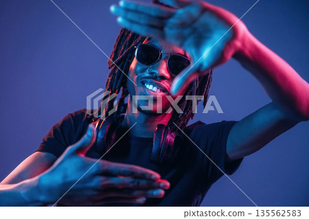 Gesture of capturing the photo. African American guy is studio with neon lighting 135562583