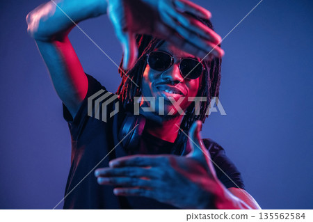 Gesture of capturing the photo. African American guy is studio with neon lighting Gesture of capturing the photo. African American guy is studio with neon lighting 135562584