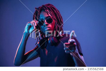 Pointing by finger, in sunglasses. African American guy is studio with neon lighting 135562588