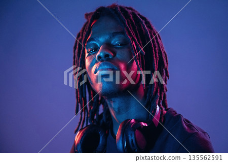 Serious, headphones on the neck. African American guy is studio with neon lighting 135562591