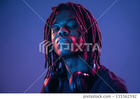 Serious, headphones on the neck. African American guy is studio with neon lighting 135562592