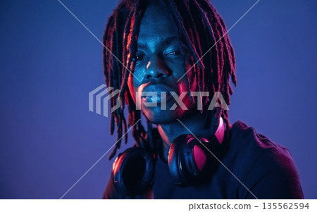 Serious, headphones on the neck. African American guy is studio with neon lighting 135562594