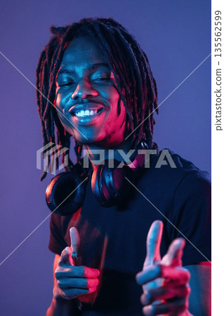 Friendly and cheerful facial expression. African American guy is studio with neon lighting Friendly and cheerful facial expression. African American guy is studio with neon lighting 135562599