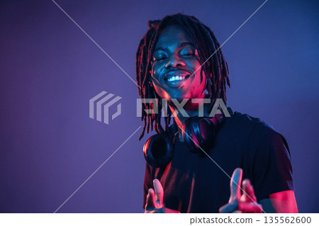 Friendly and cheerful facial expression. African American guy is studio with neon lighting Friendly and cheerful facial expression. African American guy is studio with neon lighting 135562600