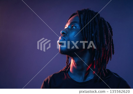 Focused close up view. African American guy is studio with neon lighting Focused close up view. African American guy is studio with neon lighting 135562620
