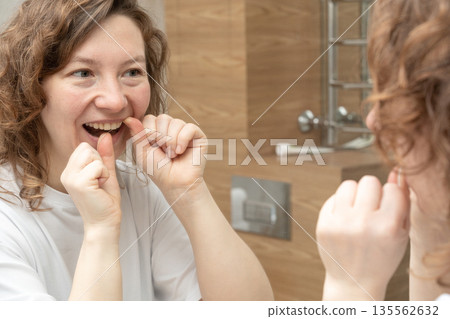 Woman performing daily dental flossing in the bathroom, maintaining good oral hygiene for a healthy smile Woman performing daily dental flossing in the bathroom, maintaining good oral hygiene for a healthy smile 135562632