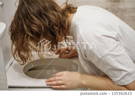Woman experiencing sickness and stomach pain, leaning over toilet bowl Woman experiencing sickness and stomach pain, leaning over toilet bowl 135562633
