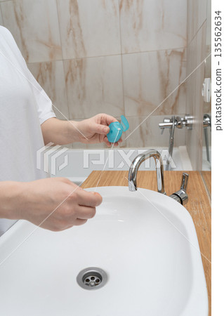Person's hands preparing dental floss over a bathroom sink, promoting daily oral care and healthy routine. Person's hands preparing dental floss over a bathroom sink, promoting daily oral care and healthy routine. 135562634