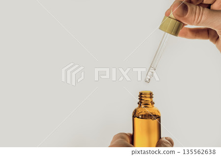 Hand holding brown glass bottle with dropper dispensing drops of serum Hand holding brown glass bottle with dropper dispensing drops of serum 135562638