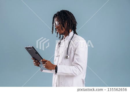 Holding notepad, doctor. Black man is in the studio against soft background Holding notepad, doctor. Black man is in the studio against soft background 135562656