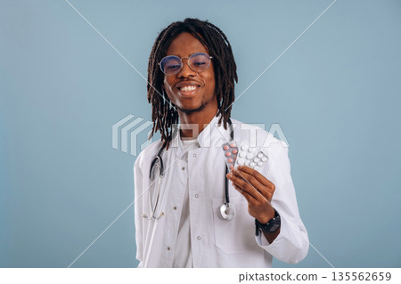 Tablets in a blister. Black man is in the studio against soft background Tablets in a blister. Black man is in the studio against soft background 135562659