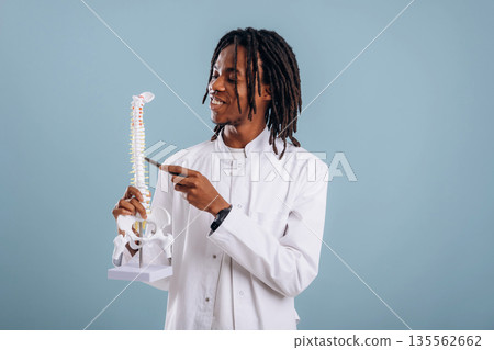 Holding human spine model, education. Black man is in the studio against soft background Holding human spine model, education. Black man is in the studio against soft background 135562662