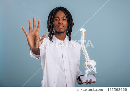 Education concept, human spine model. Black man is in the studio against soft background Education concept, human spine model. Black man is in the studio against soft background 135562666