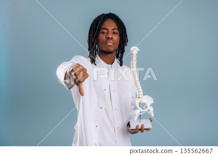 Education concept, human spine model. Black man is in the studio against soft background Education concept, human spine model. Black man is in the studio against soft background 135562667