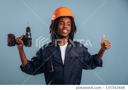 Orange hard hat and drill. Black man is in the studio against soft background Orange hard hat and drill. Black man is in the studio against soft background 135562686