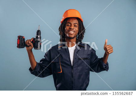 Orange hard hat and drill. Black man is in the studio against soft background Orange hard hat and drill. Black man is in the studio against soft background 135562687
