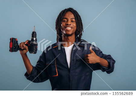 Drill in hand, worker. Black man is in the studio against soft background 135562689