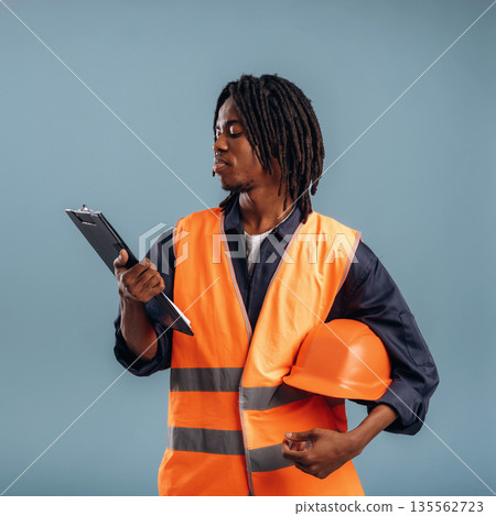 Construction worker, with notepad and hard hat. Black man is in the studio against soft background 135562723