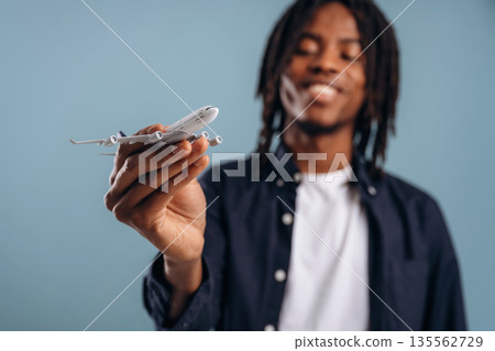 Travel conception, holding little plane. Black man is in the studio against soft background Travel conception, holding little plane. Black man is in the studio against soft background 135562729