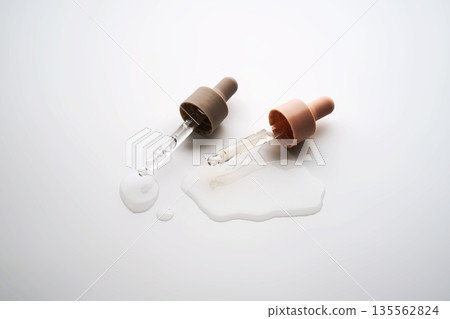 Cosmetic serum droppers dispensing liquid on white surface Cosmetic serum droppers dispensing liquid on white surface 135562824