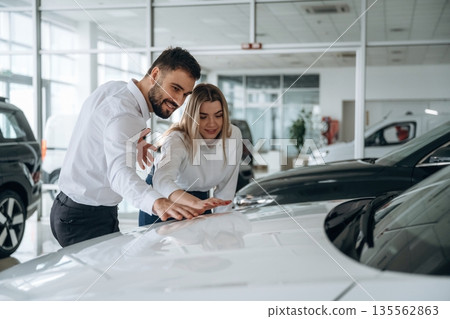 Showing the new product. Man and woman are in the car dealership 135562863