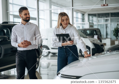 Black notepad in hands. Man and woman are in the car dealership Black notepad in hands. Man and woman are in the car dealership 135562875