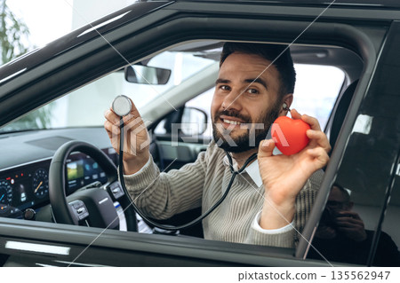 Stethoscope and red little heart model. Man is with the car in dealership 135562947