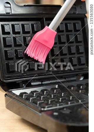 Oiling the surface of the waffle iron, preparing for baking homemade waffles. Oiling the surface of the waffle iron, preparing for baking homemade waffles. 135563080