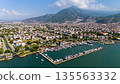 Aerial view of Fethiye marina with boats, coastal city and mountains. Mediterranean waterfront with harbor, residential areas and green hills in Turkey. 135563332