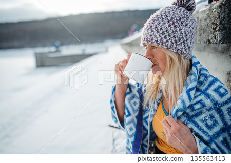 Older woman enyoing hot tea after ice bathing in lake. 135563413