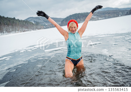 Elderly woman practicing outdoor ice bathing during winter season 135563415