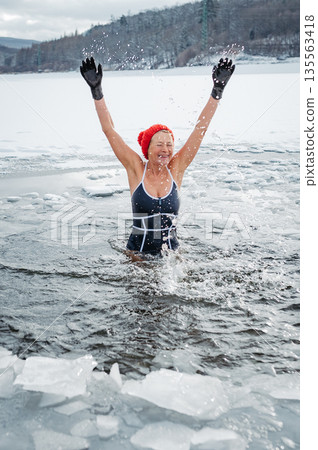Elderly woman practicing outdoor ice bathing during winter season 135563418