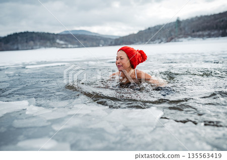 Elderly woman practicing outdoor ice bathing during winter season 135563419
