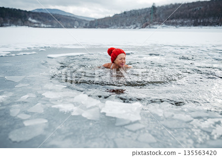 Elderly woman practicing outdoor ice bathing during winter season 135563420