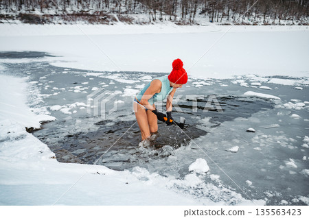 Senior woman breaking ice for winter swimming on frozen lake. Senior woman breaking ice for winter swimming on frozen lake. 135563423