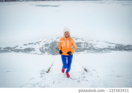 Active elderly woman jogging in cold snowy weather. 135563431
