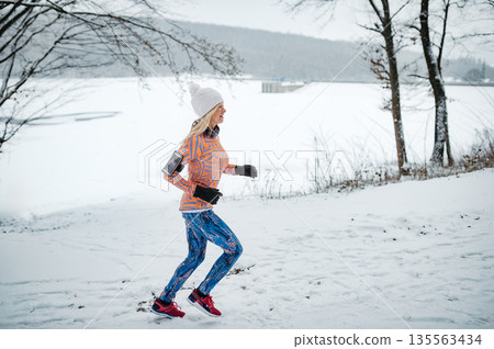 Active elderly woman jogging in cold snowy weather. 135563434
