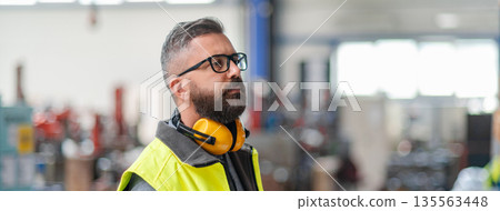 Warehouse or factory worker with protective earmuffs. Warehouse or factory worker with protective earmuffs. 135563448
